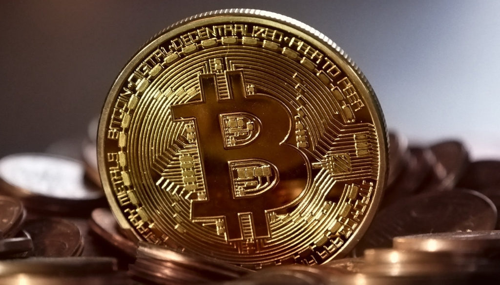 A shiny gold Bitcoin coin stands upright among stacks of coins, symbolizing cryptocurrency and Wisconsin accounting services.