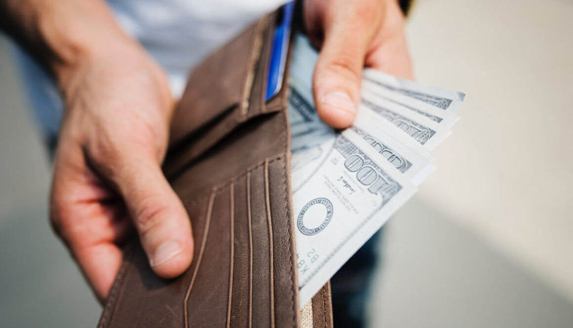 Hands holding an open wallet with hundred-dollar bills, representing smart financial planning by fiduciary advisors in Wisconsin.
