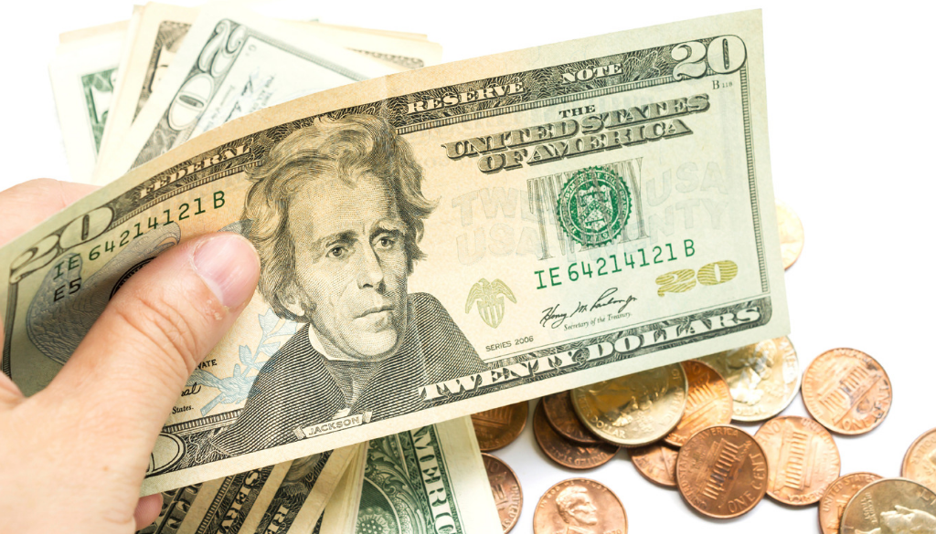 A hand holds US dollar bills above coins, representing tax planning and accounting services by fiduciary advisors in Wisconsin.