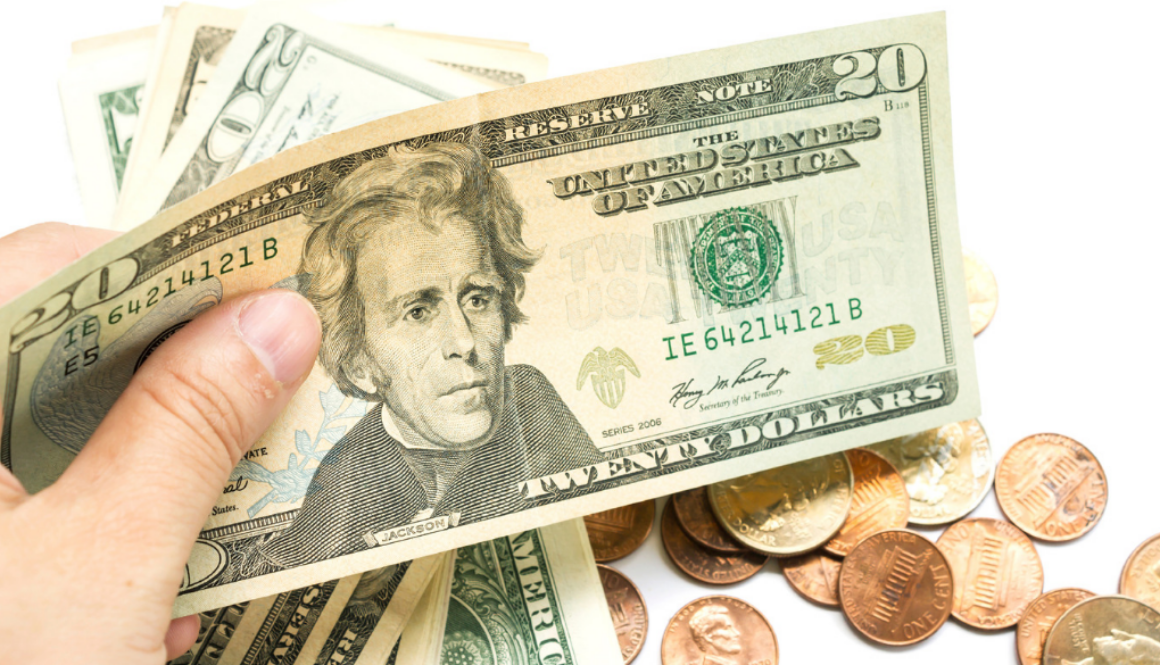 A hand holds US dollar bills above coins, representing tax planning and accounting services by fiduciary advisors in Wisconsin.