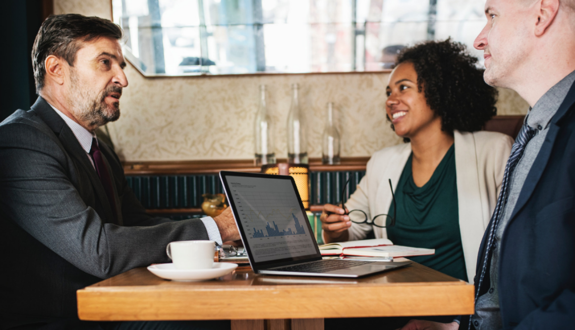 Three professionals discuss tax planning at a café table with a laptop and coffee, representing Advisors Management Group in Wisconsin.