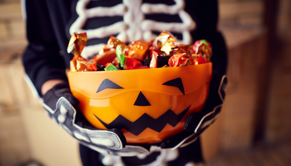A child in a skeleton costume holds a pumpkin-shaped bowl of Halloween candy in Wisconsin, home to Advisors Management Group.
