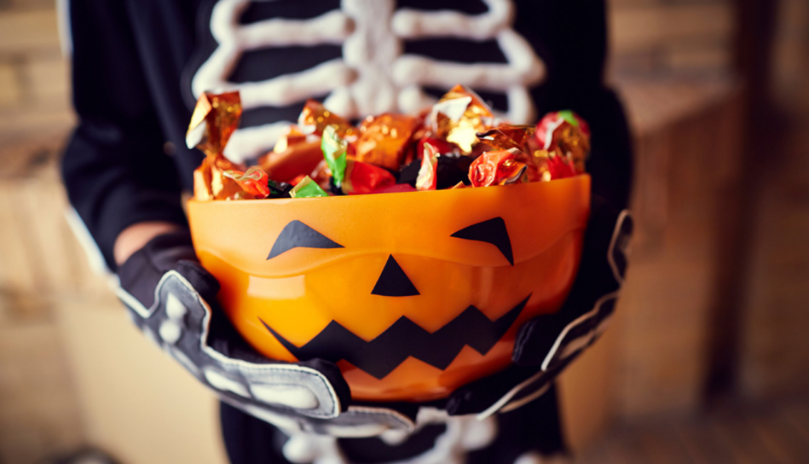 A child in a skeleton costume holds a pumpkin-shaped bowl of Halloween candy in Wisconsin, home to Advisors Management Group.