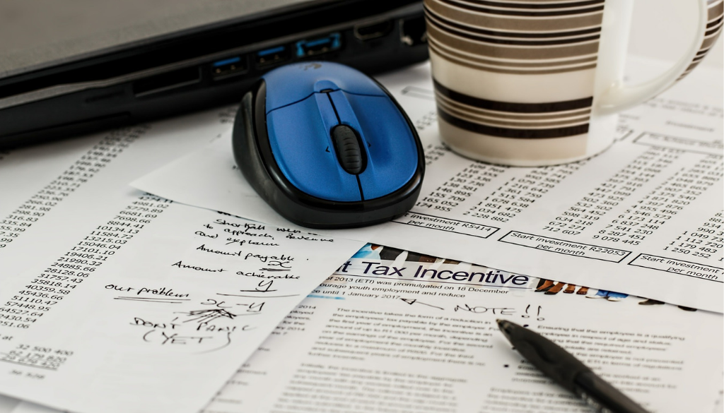 Tax planning documents with handwritten notes, a pen, blue mouse, and mug on a Wisconsin fiduciary advisor’s desk.