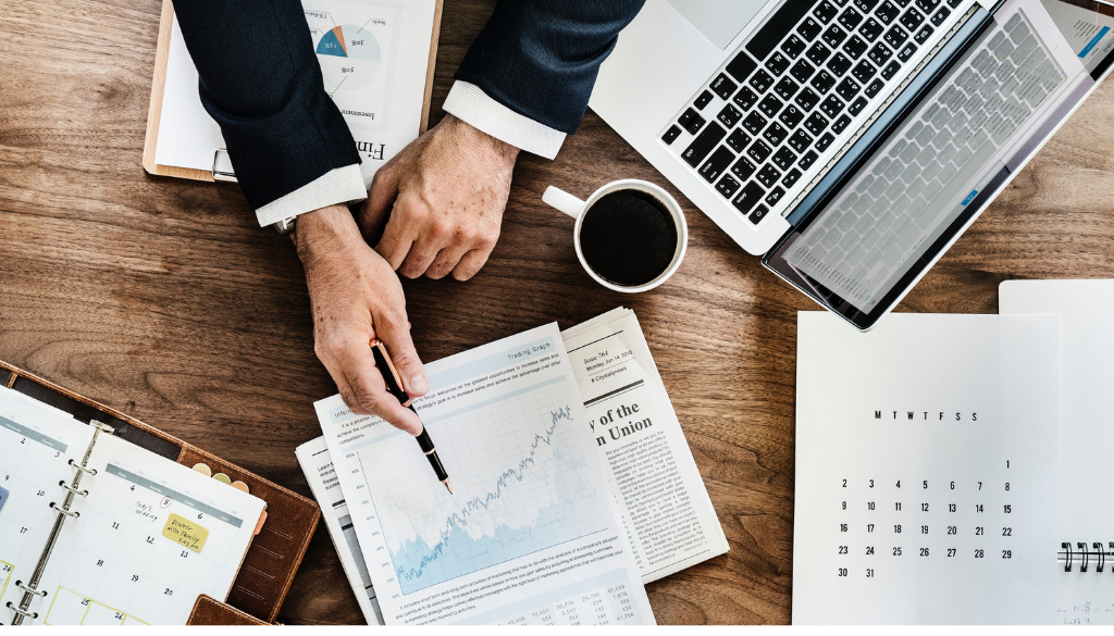 A person reviews financial charts for tax planning at a desk with a laptop, planner, and coffee at Advisors Management Group in Wisconsin.