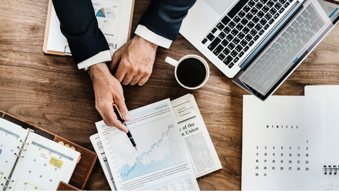 A person reviews financial charts for tax planning at a desk with a laptop, planner, and coffee at Advisors Management Group in Wisconsin.