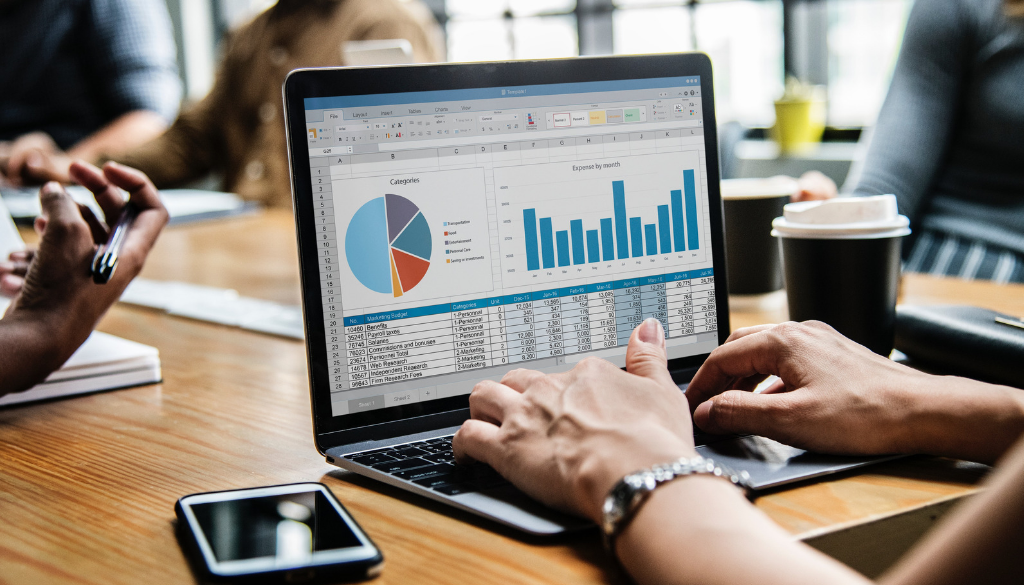 A person in Wisconsin uses a laptop for financial planning with charts, spreadsheets, coffee, and a smartphone at a work desk.