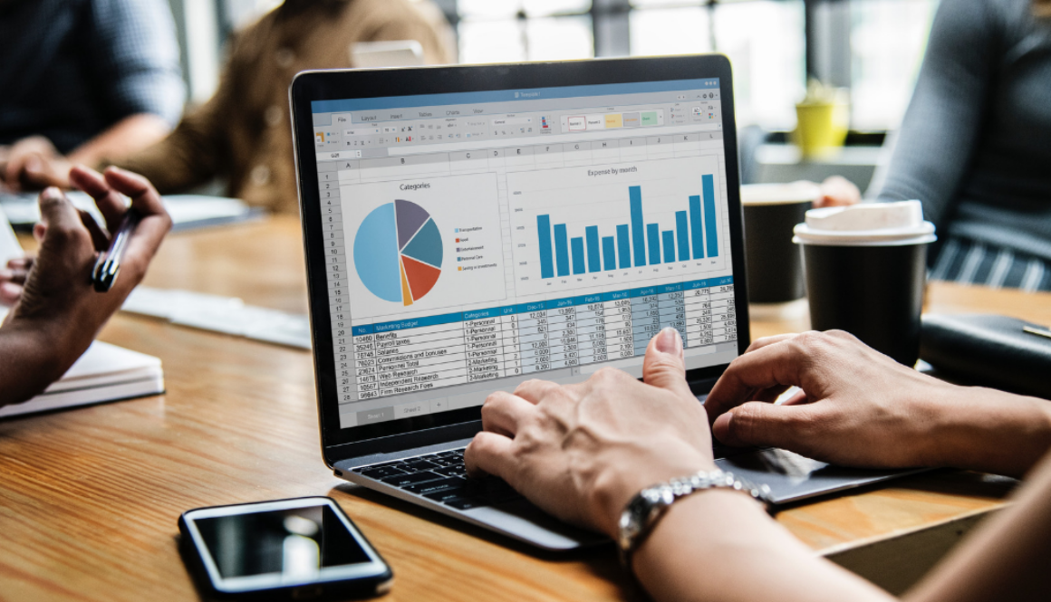 A person in Wisconsin uses a laptop for financial planning with charts, spreadsheets, coffee, and a smartphone at a work desk.