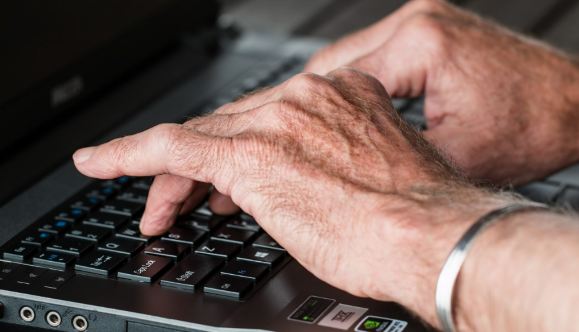 Close-up of elderly hands typing on a laptop, symbolizing fiduciary financial advisors in Wisconsin at Advisors Management Group.