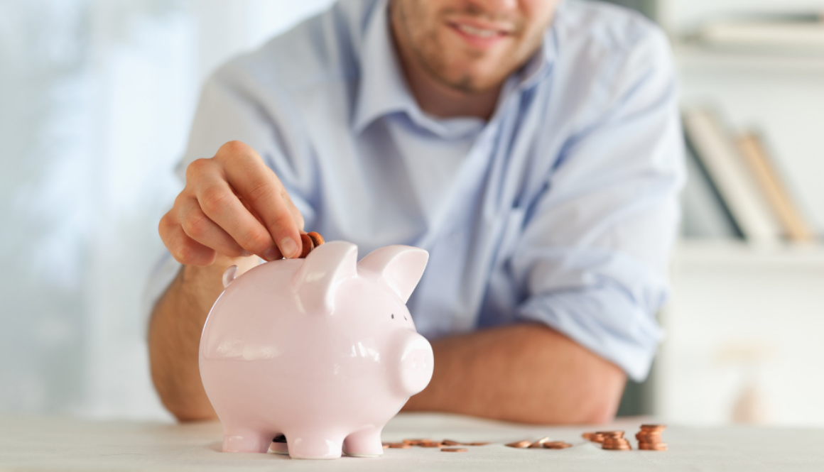 A man adds coins to a pink piggy bank on a table, symbolizing careful financial planning with fiduciary advisors in Wisconsin.
