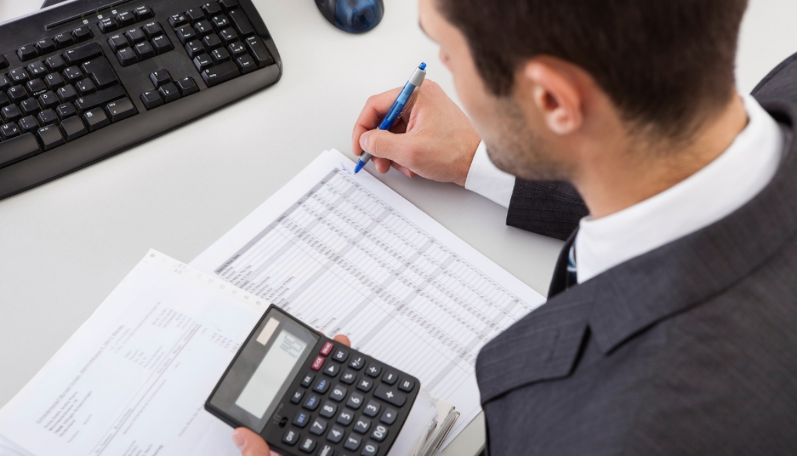 Fiduciary financial advisor in Wisconsin reviews tax planning documents and uses a calculator at a desk with a keyboard.
