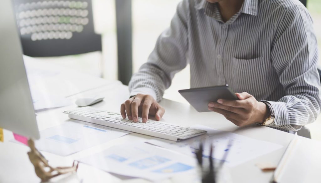 A person in a striped shirt uses a keyboard and tablet to research financial planning with Advisors Management Group in Wisconsin.