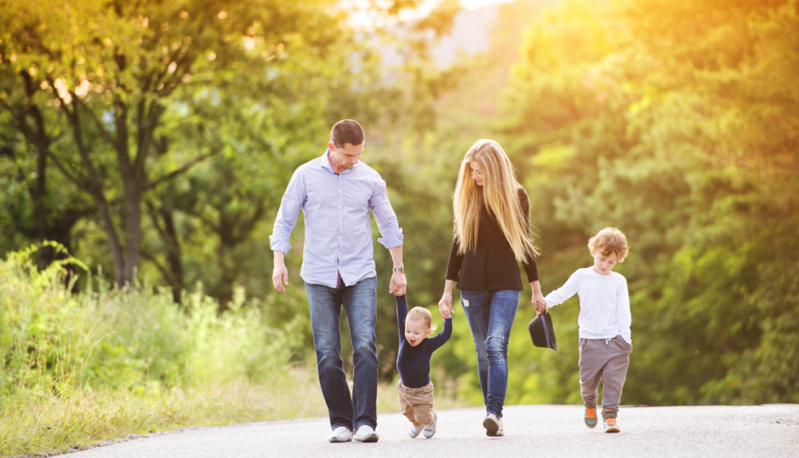 A family of four walks hand in hand on a sunny day, representing fiduciary financial advisors in Wisconsin guiding your future.