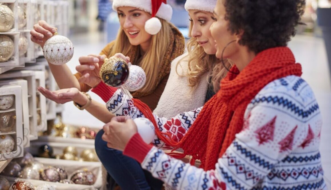 Three women in festive sweaters and Santa hats shop for Christmas ornaments together in Wisconsin, home to Advisors Management Group.
