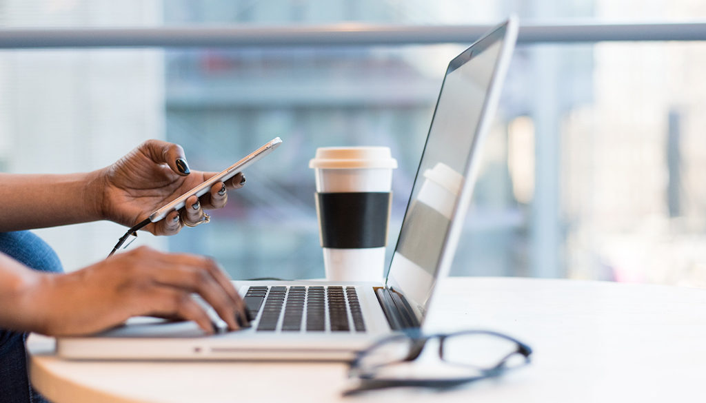A person reviews Wisconsin accounting services on a laptop and smartphone at a table with coffee and eyeglasses.