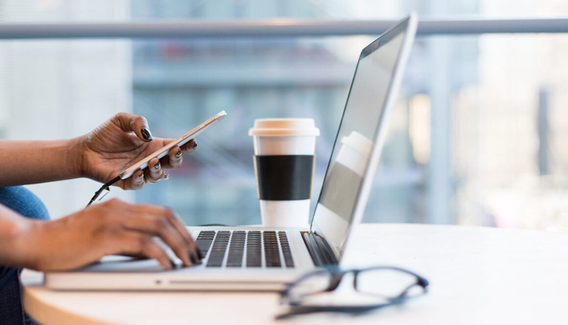 A person reviews Wisconsin accounting services on a laptop and smartphone at a table with coffee and eyeglasses.
