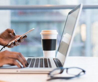 A person reviews Wisconsin accounting services on a laptop and smartphone at a table with coffee and eyeglasses.
