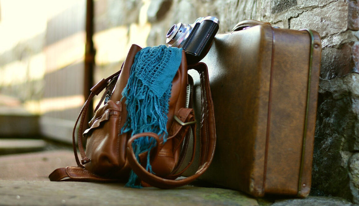 A brown backpack and suitcase with a teal scarf and camera by a stone wall inspire Wisconsin travelers to consider tax planning.