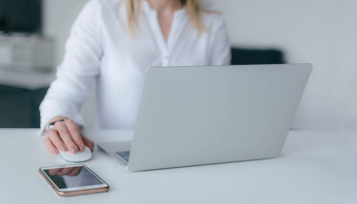 A person in a white shirt works on a laptop with a smartphone nearby in a bright, minimal Wisconsin fiduciary advisory office.