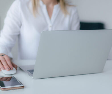 A person in a white shirt works on a laptop with a smartphone nearby in a bright, minimal Wisconsin fiduciary advisory office.