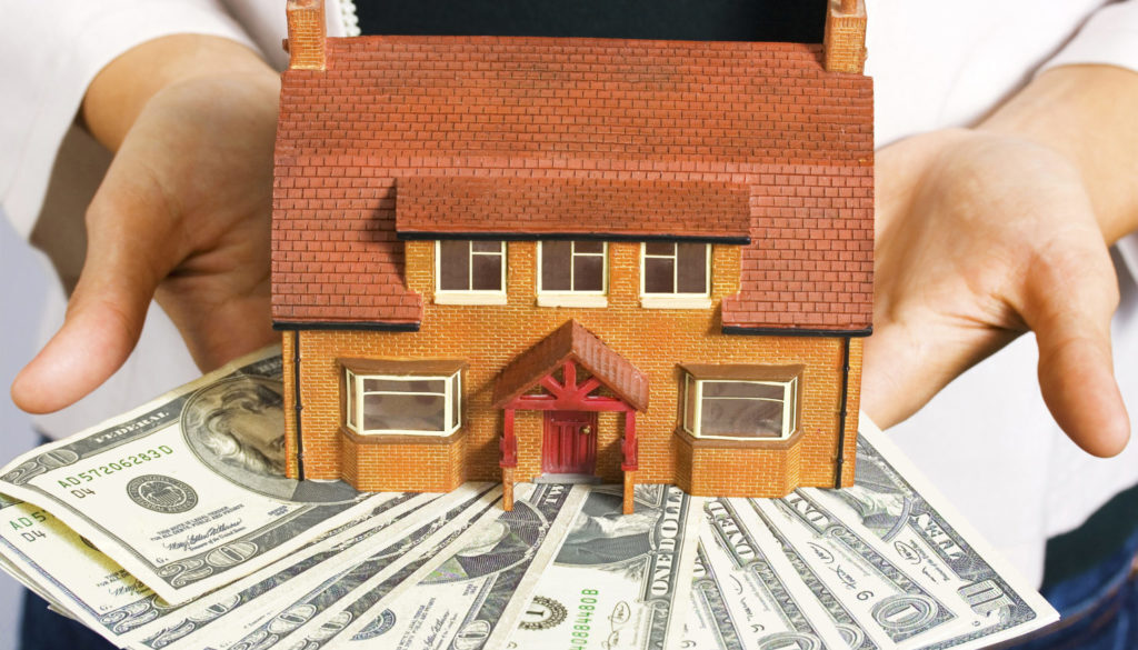A person holds a model house above scattered US dollar bills, symbolizing financial planning and investment advisory in Wisconsin.