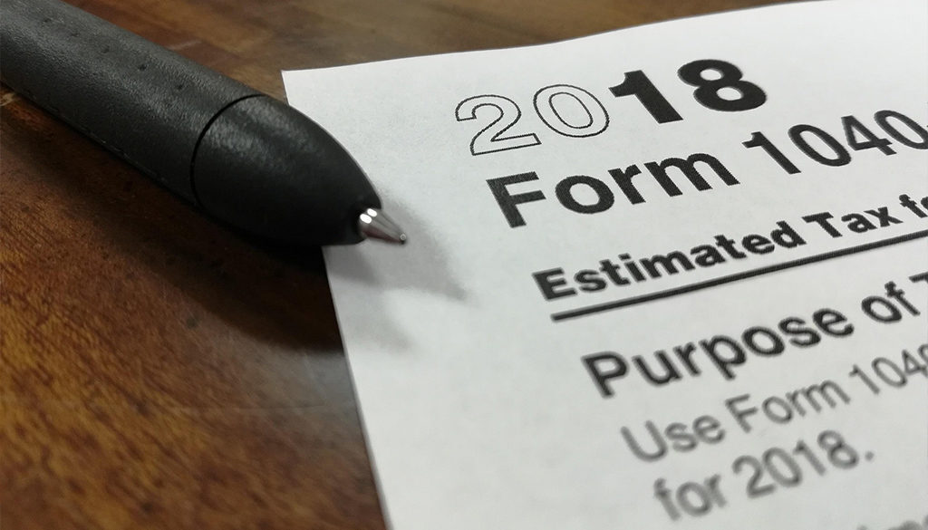 A black pen lies on a wooden desk next to a 2018 Form 1040, highlighting tax planning for Wisconsin financial advisors.