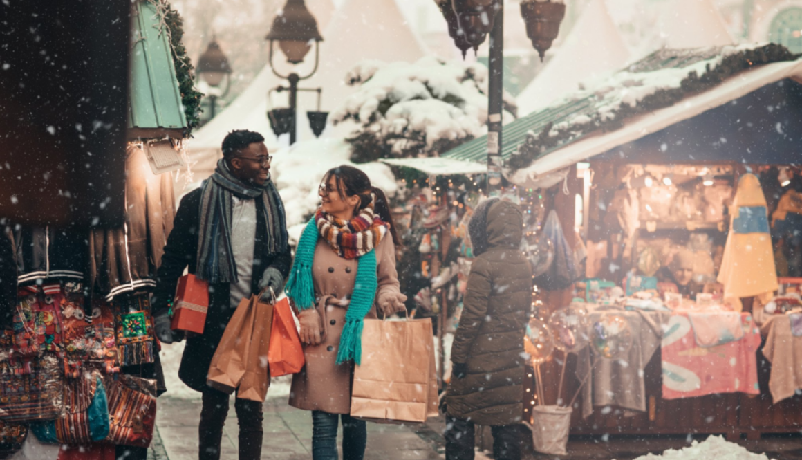 A couple carrying shopping bags enjoys a snowy Wisconsin holiday market, reflecting the warmth of local communities we serve.