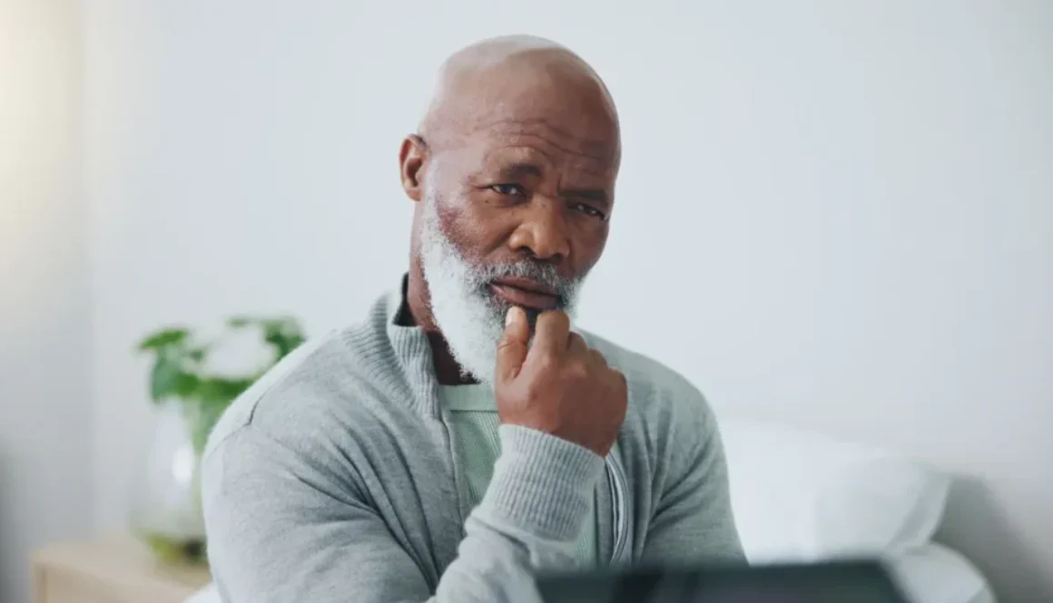 Man with gray beard looking thoughtful while resting chin on hand.