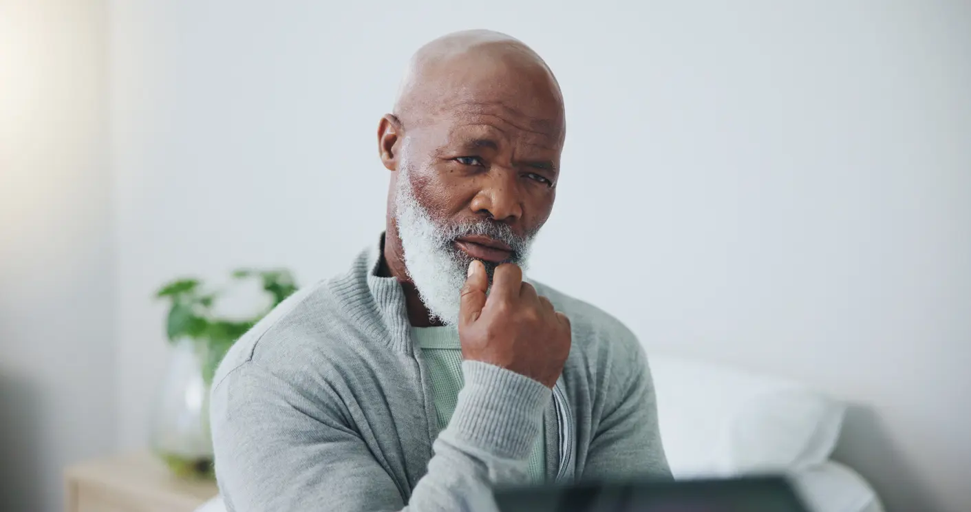 Man with gray beard looking thoughtful while resting chin on hand.