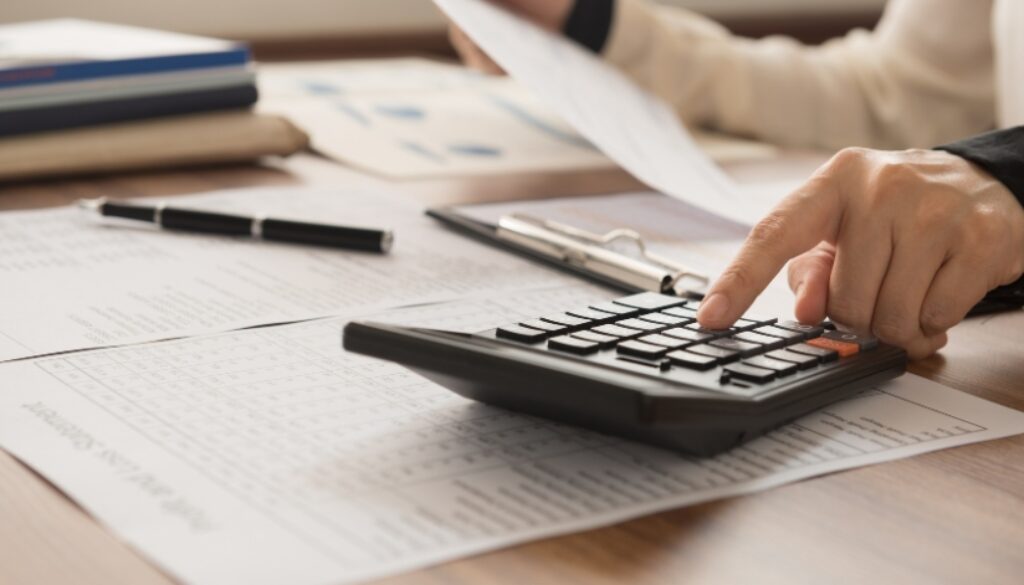 Person reviewing tax documents while punching numbers into a calculator.