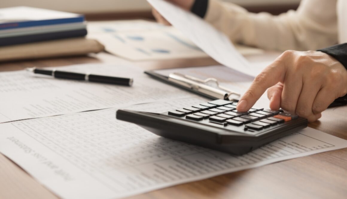 Person reviewing tax documents while punching numbers into a calculator.