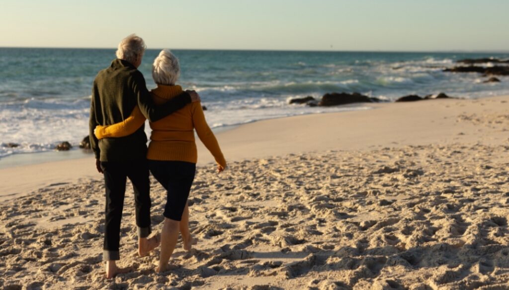 Elderly couple with their arms around each other walking on the beach.