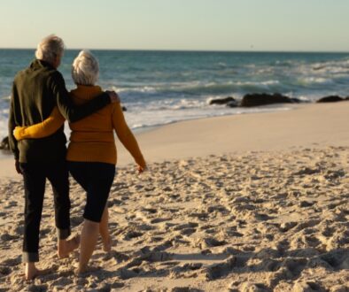 Elderly couple with their arms around each other walking on the beach.