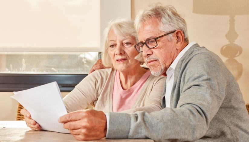 An elderly couple sitting at a table reviewing paperwork documents.