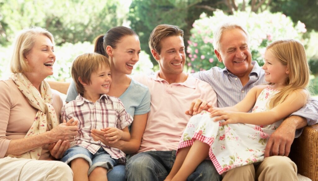 A family sitting on an outdoor patio with grandparents, parents, and grandchildren, laughing.