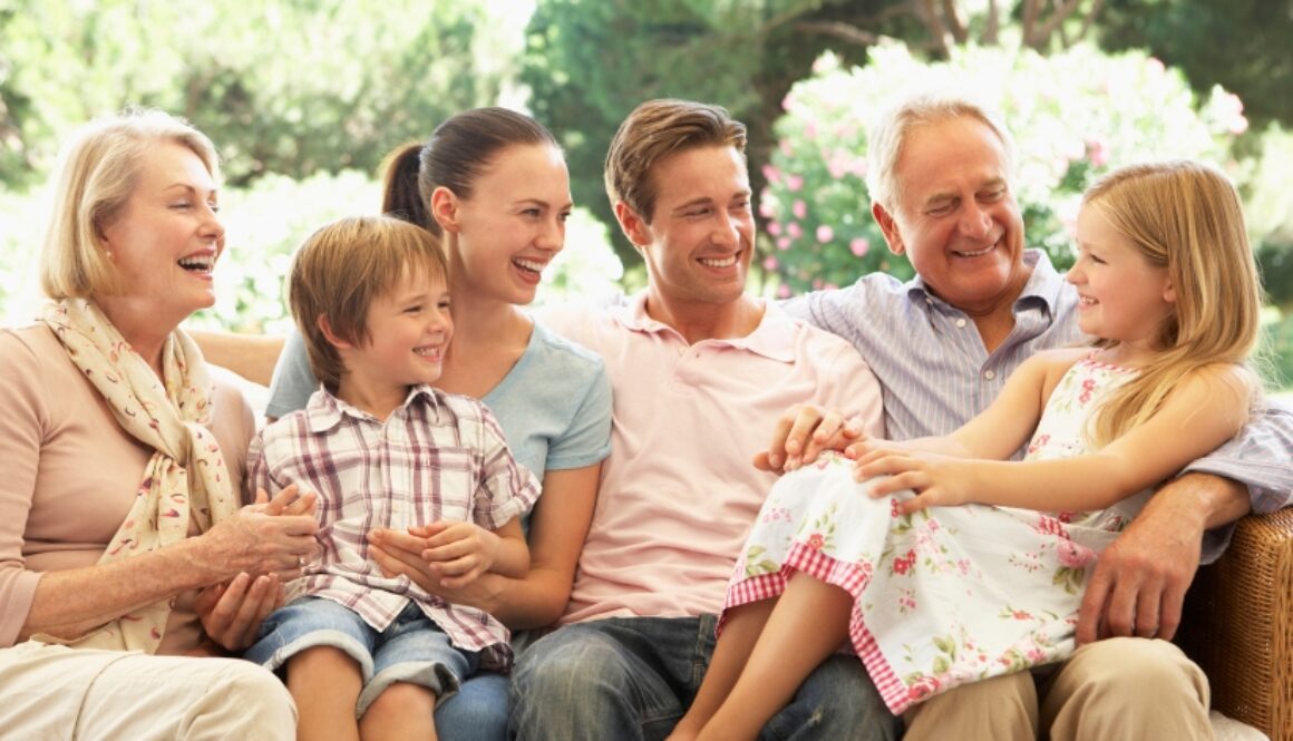 A family sitting on an outdoor patio with grandparents, parents, and grandchildren, laughing.