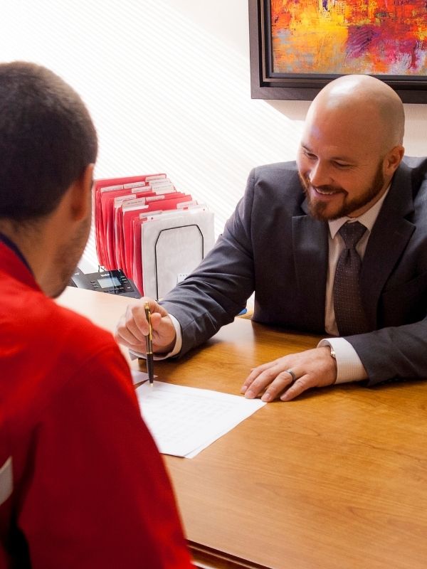 Warren Deets, a AMG fiduciary financial advisor in La Crosse, Wisconsin. smiles while helping a client with financial planning paperwork at a desk.