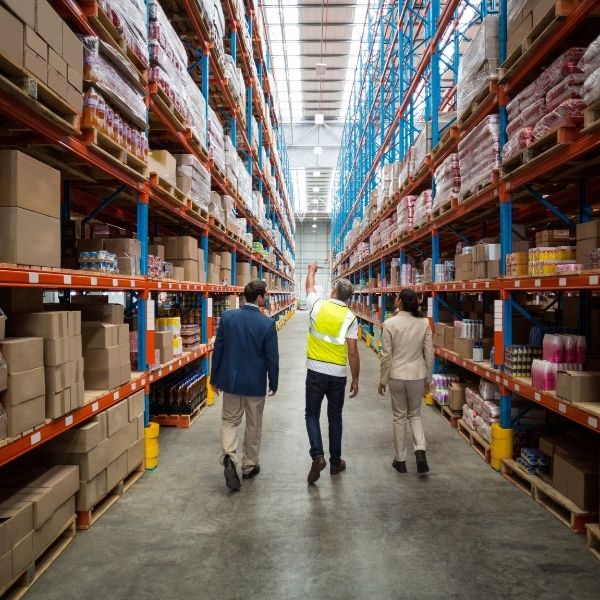 Three people walk down an aisle in a large Wisconsin warehouse, reflecting business consulting and financial advisory services.
