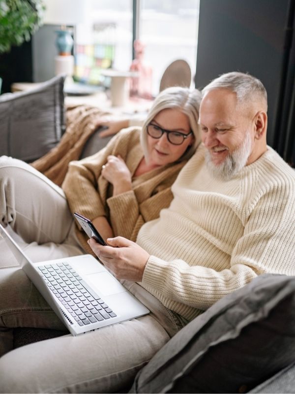 An older couple in Wisconsin smiles on a couch, using a laptop for financial planning with fiduciary advisors from Advisors Management Group.