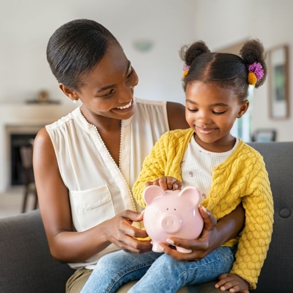 A smiling woman and young girl build smart financial planning habits at home by putting coins in a piggy bank in Wisconsin.