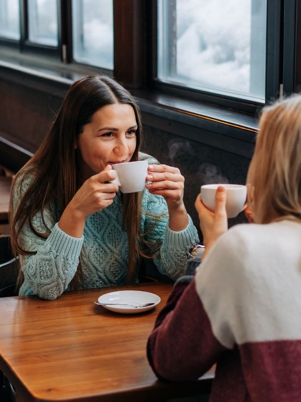 Two women discuss financial planning over coffee at a wooden table in Wisconsin, meeting with a fiduciary advisor by a window.