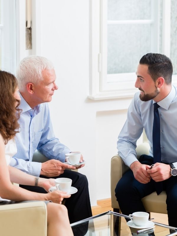 Three professionals discuss tax planning over coffee in a modern office at Advisors Management Group, fiduciary advisors in Wisconsin.