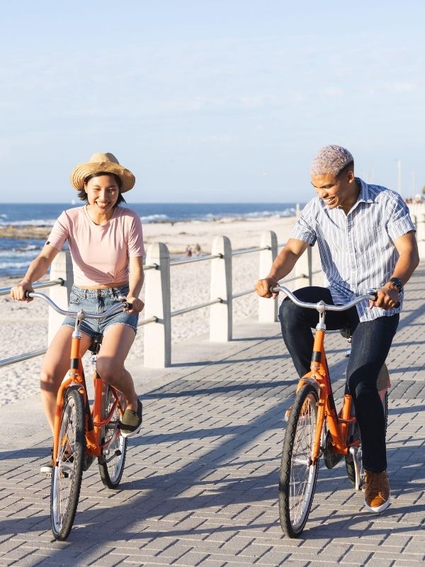 Two people enjoy a sunny day riding orange bicycles along a Wisconsin beachside path, symbolizing financial freedom and planning.
