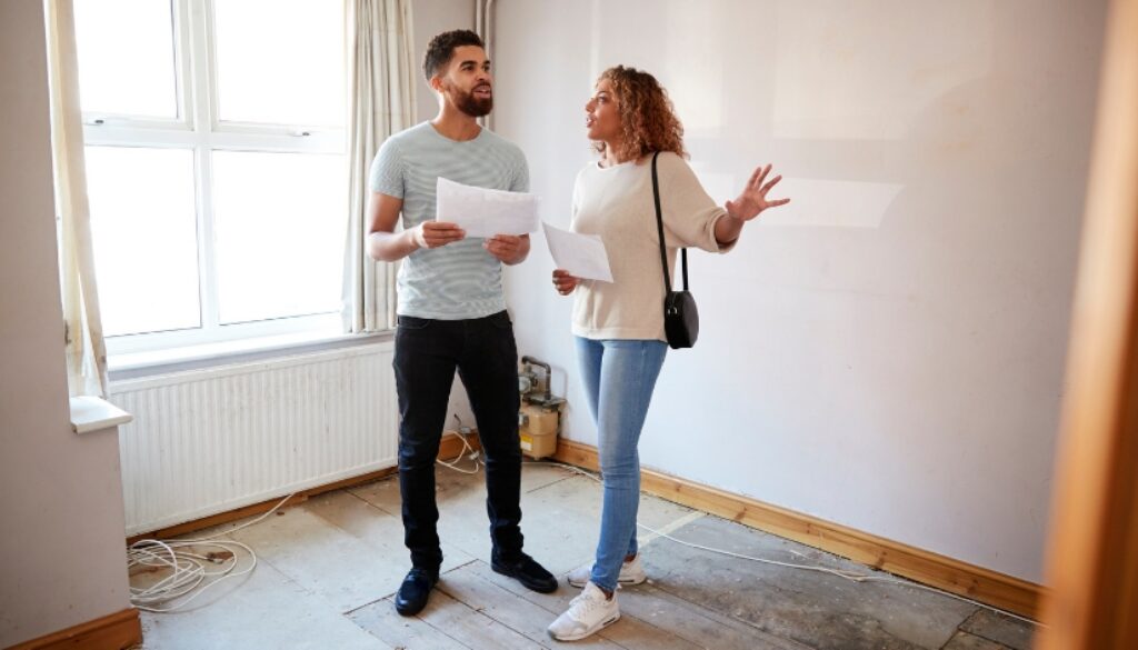 A couple holding financial documents in an empty room while house shopping.