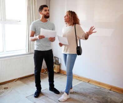 A couple holding financial documents in an empty room while house shopping.