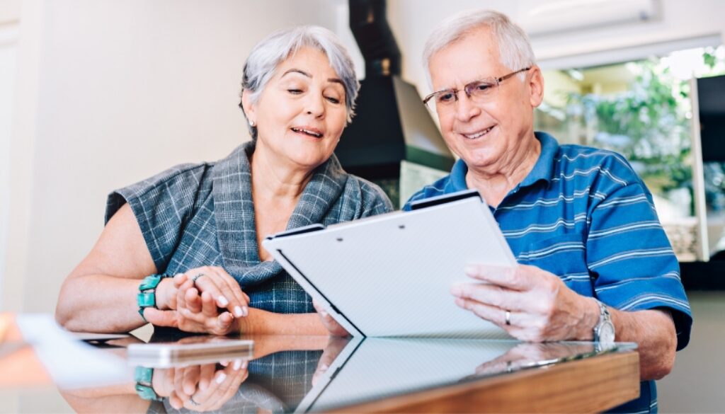 Elderly couple reviewing paperwork at kitchen table.
