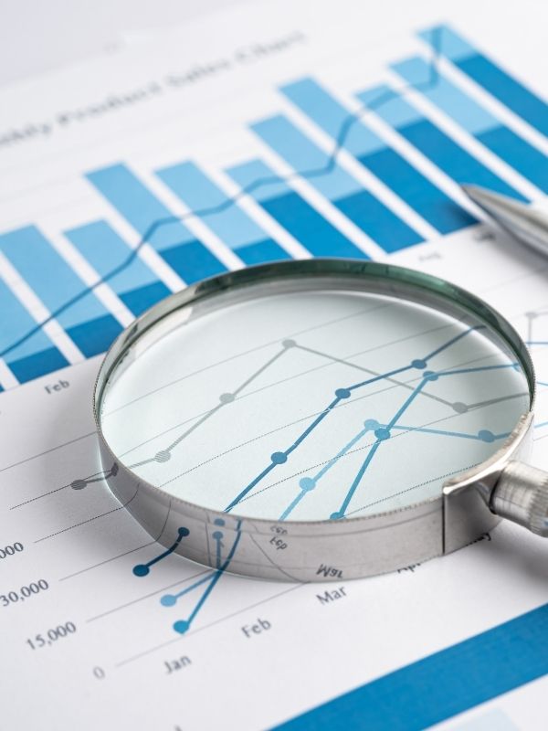 A magnifying glass highlights a line graph and bar charts, representing financial data and accounting analysis for Wisconsin advisors.