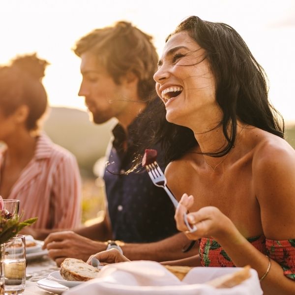 A woman laughs with friends at a sunlit outdoor meal as they discuss tax planning in Wisconsin with fiduciary financial advisors.