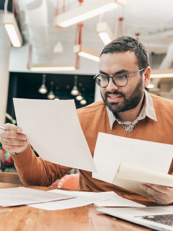 A man in glasses and a brown sweater reviews financial planning papers at his desk in a modern Wisconsin advisory office.
