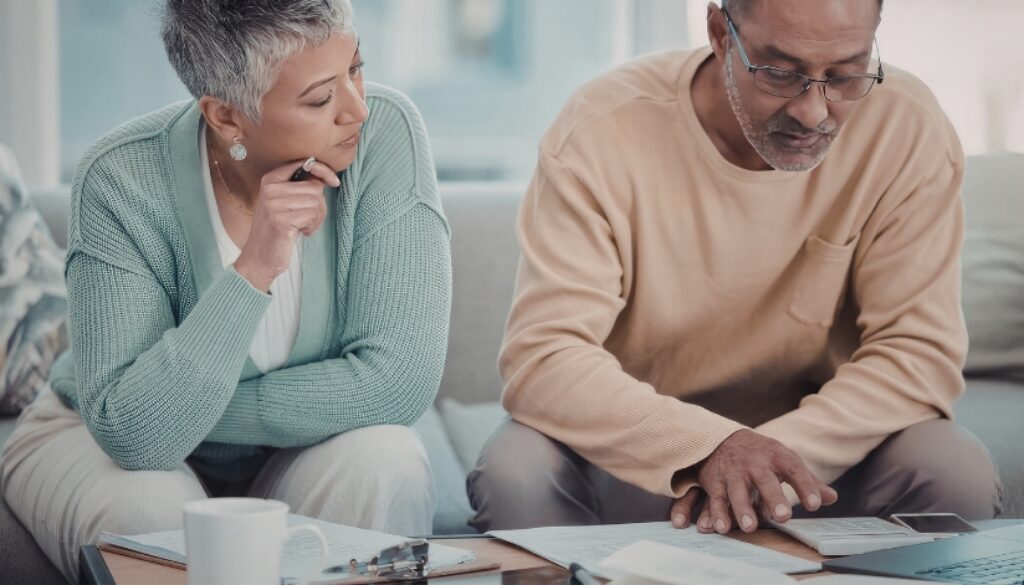 A couple sitting at their coffee table looking at financial documents and using a calculator.